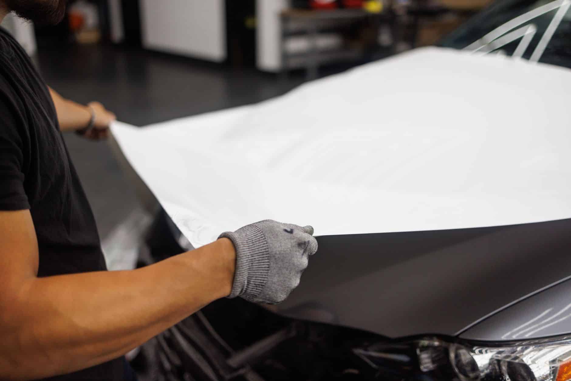 Technician applying color PPF film to a luxury car hood in a climate-controlled studio